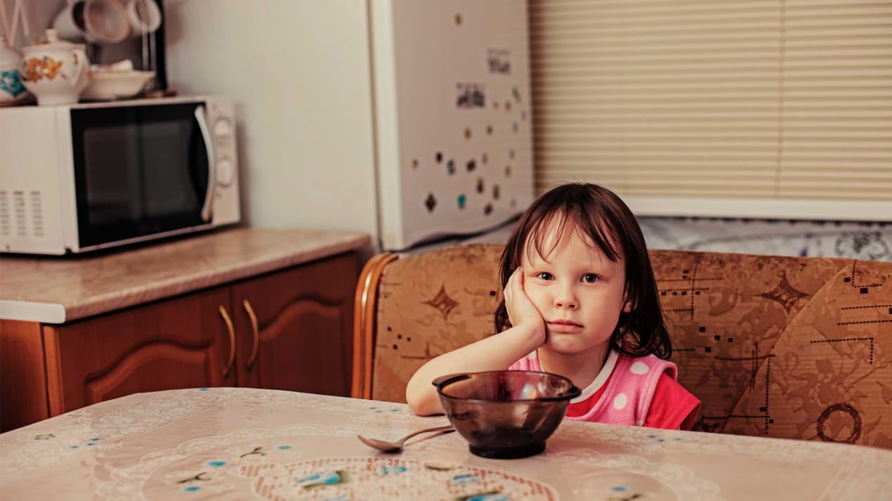 Ein enttäuscht wirkendes kleines Mädchen an einem Esstisch vor einer leeren Glasschüssel