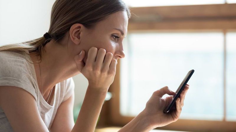 Eine junge, gelangweilt aussehende Frau schaut auf ein Smartphone