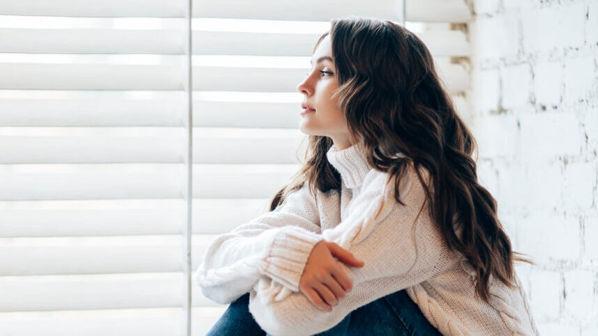 Junge Frau sitzt alleine auf einer Fensterbank