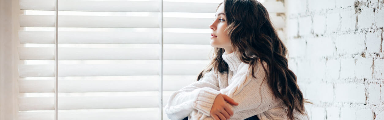 Junge Frau sitzt alleine auf einer Fensterbank