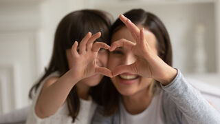 Ein Kind und eine junge Frau formen mit den Fingern ein Herz.