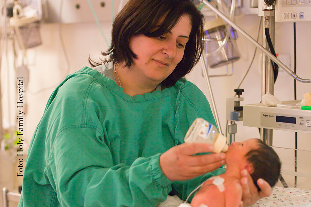 Krankenschwester im grünen Kittel füttert Baby mit Fläschchen