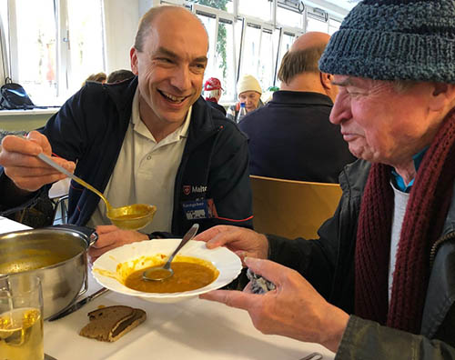 Ein Mann bietet einem anderen Mann einen Teller Suppe an