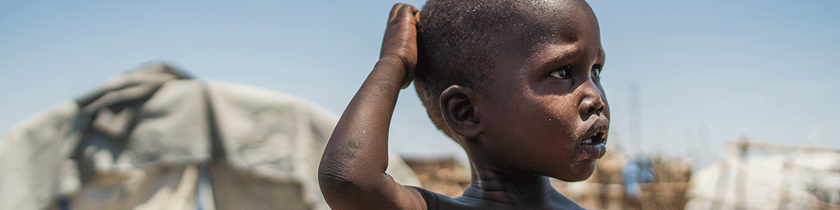 Kleiner Junge aus Ostafrika kratzt sich am Kopf und blickt in die Ferne