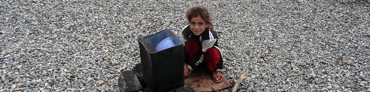 Kleines syrisches Mädchen sitzt neben Mülleimer auf Kiesboden