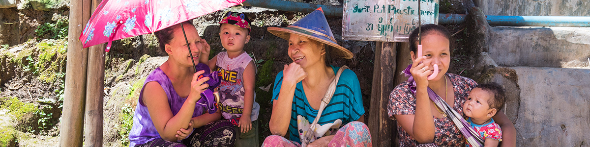 Asiatische Frauen sitzen mit Kleinkindern unter Sonnenschirmen 