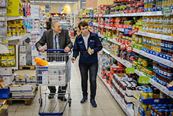 Eine Mitarbeiterin des Malteser Mobilen Einkaufswagen hilft einem älteren Mann beim Einkaufen.