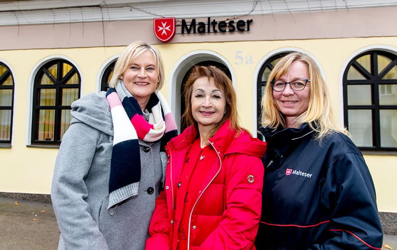 Drei lachende Frauen stehen vor der Malteser Dienststelle.