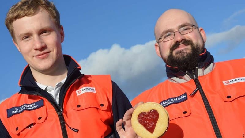 Einer vin zwei Rettungssanitätern hält einen Keks mit Marmeladen-Herz in die Kamera