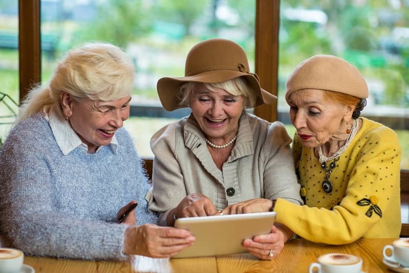 Drei ältere Damen amüsieren sich am Tablet.