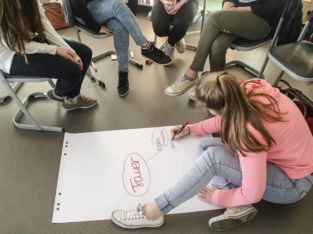 Mädchen sitzt auf dem Boden und schreibt etwas auf ein Plakat