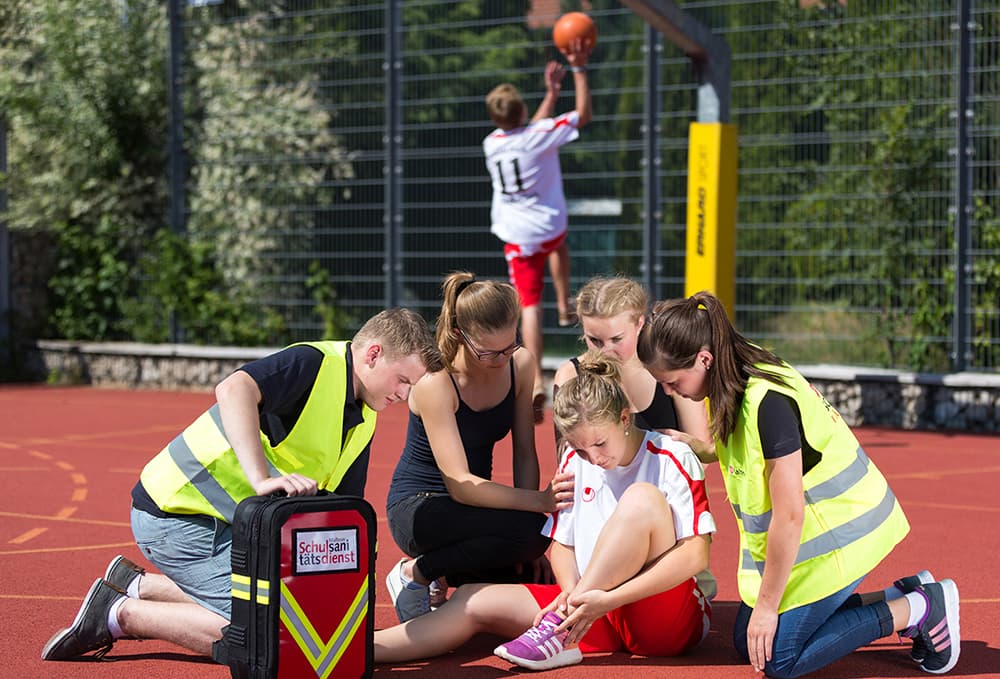 Malteser Schulsanitäter versorgen ein gestürztes Mädchen auf dem Basketballplatz