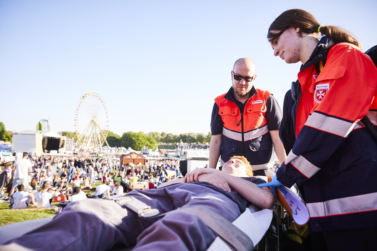 Zwei Mitarbeiter des Malteser Sanitätsdienstes kümmern sich um einen Verletzten, während einer Großveranstaltung.