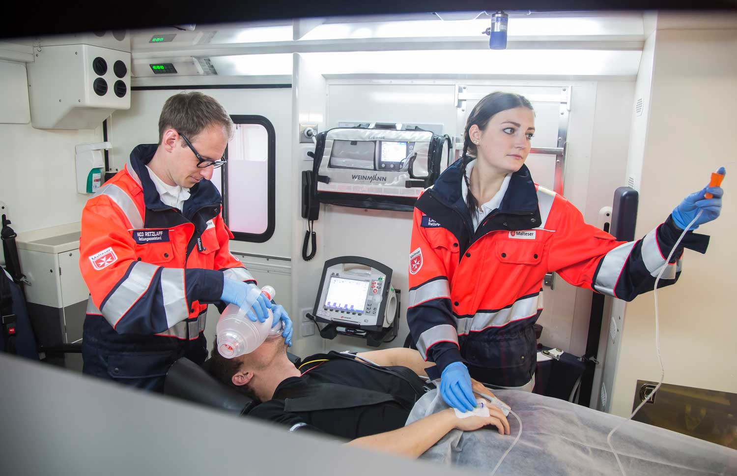 Notfallsanitäter der Malteser helfen einem Mann im Rettungswagen.