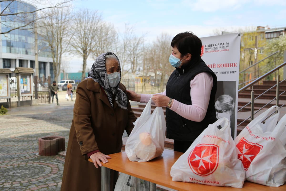 Malteser Mitarbeiterin verteilt Taschen mit Lebensmitteln an eine bedürftige ältere Frau in der Ukraine. 