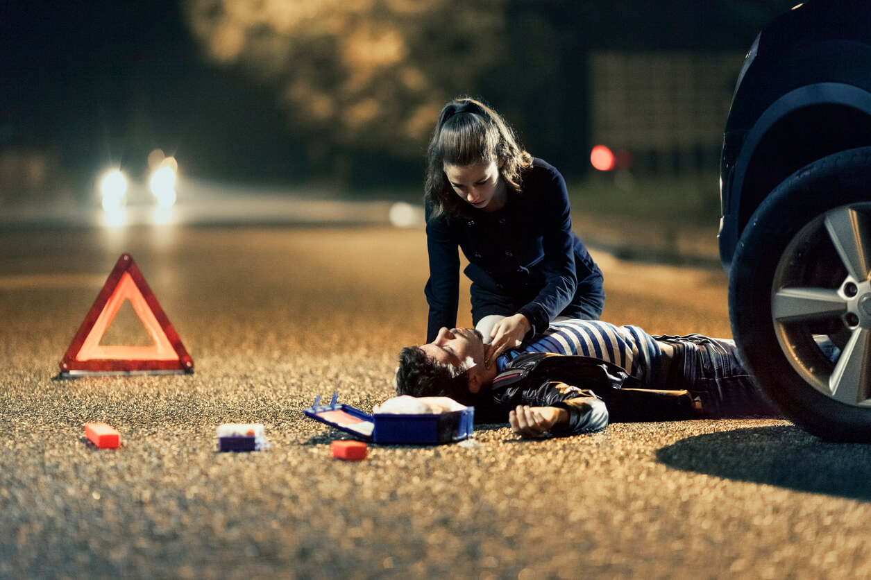 Erste Hilfe Autounfall: Junge Frau kniet über Unfallopfer und wendet Erste Hilfe Maßnahmen an