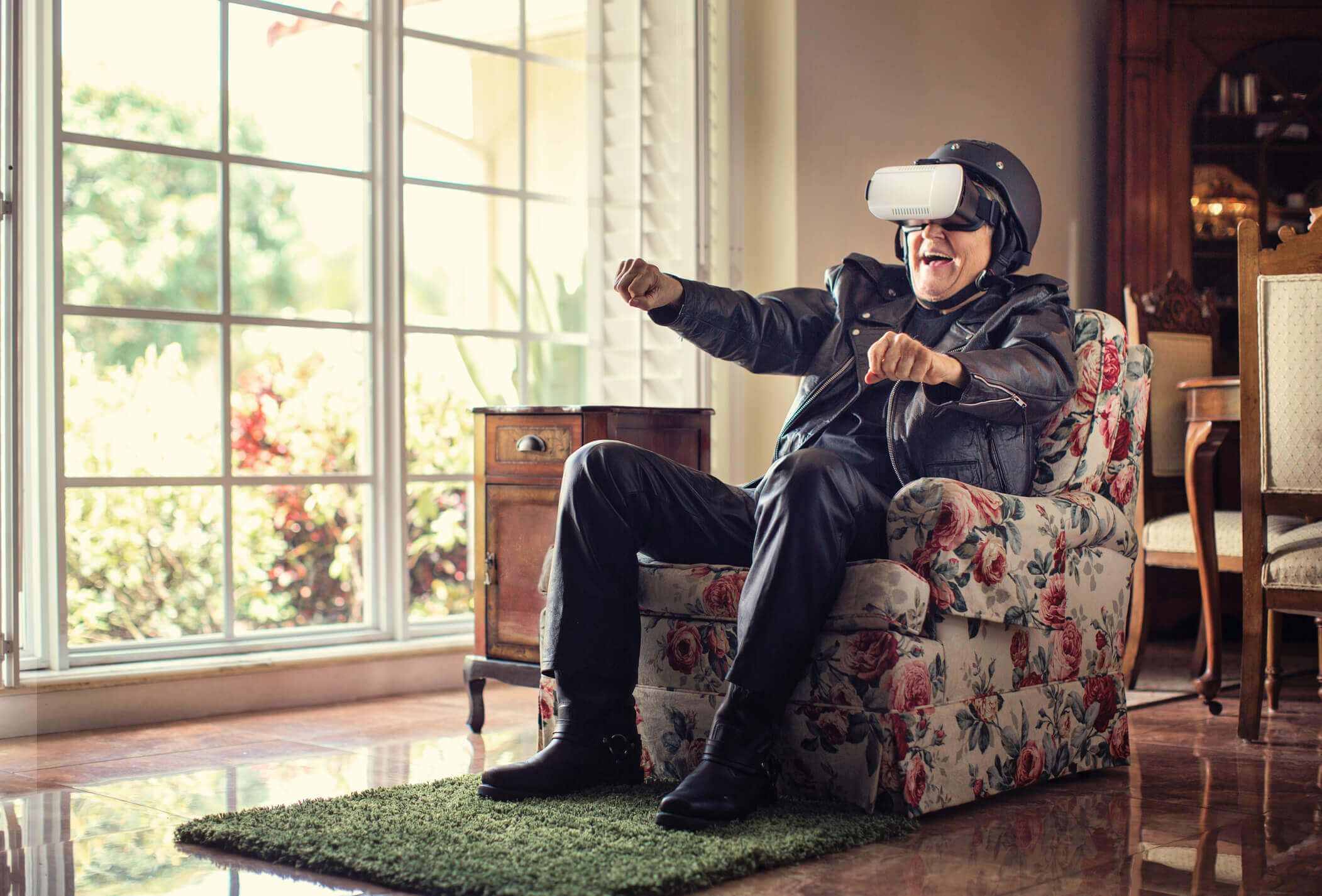 Senior sitzt auf einem Sessel und trägt eine Virtual Reality Brille