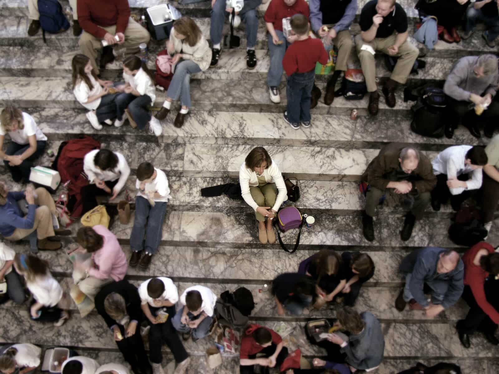 Gruppe von Menschen sitzen auf einer Treppe, eine Person sitzt isoliert