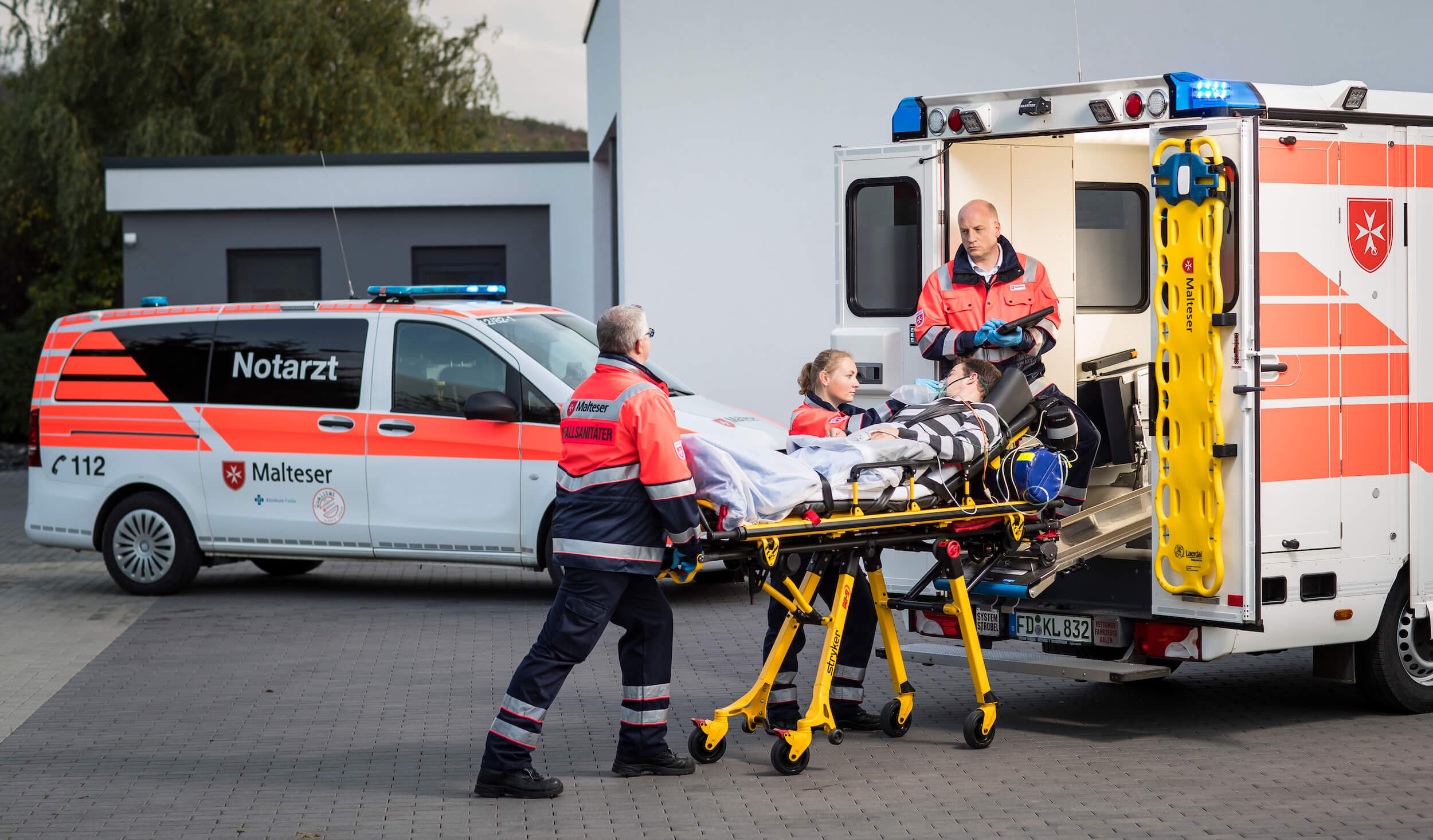 Drei Rettungsdienstsanitäter schieben Trage mit Patienten in den Rettungswagen