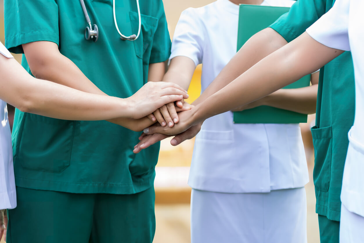 Pflegekräfte stehen im Kreis zusammen und symbolisieren Gemeinschaft, in dem sie ihre Hände zusammen aufeinanderlegen.