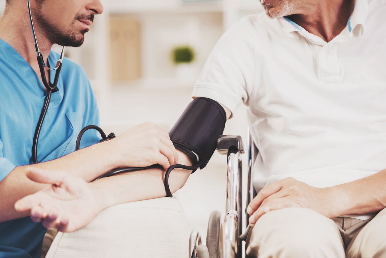 Ein Pfleger misst den Blutdruck eines älteren Rollstuhlfahrers.