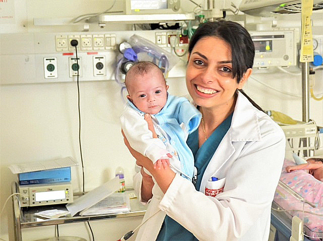 Lächelnde Ärztin hält ein Baby auf einer Säuglingsstation