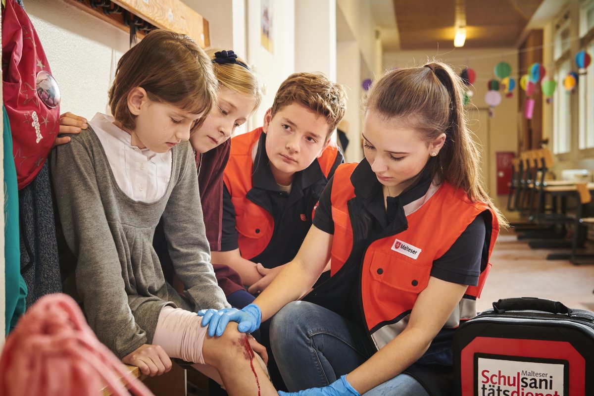 Zwei Jugendliche des Schulsanitätsdiensts behandeln das blutende Knie eines Mädchens.