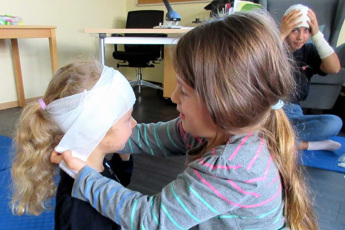 Ein junges Mädchen legt einem anderen Mädchen einen Kopfverband an.