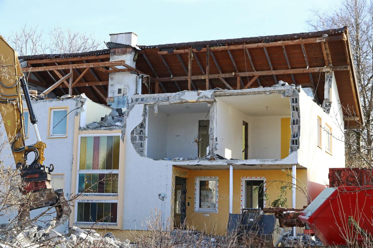 Ein stark beschädigtes Haus wird mithilfe eines Baggers abgerissen.