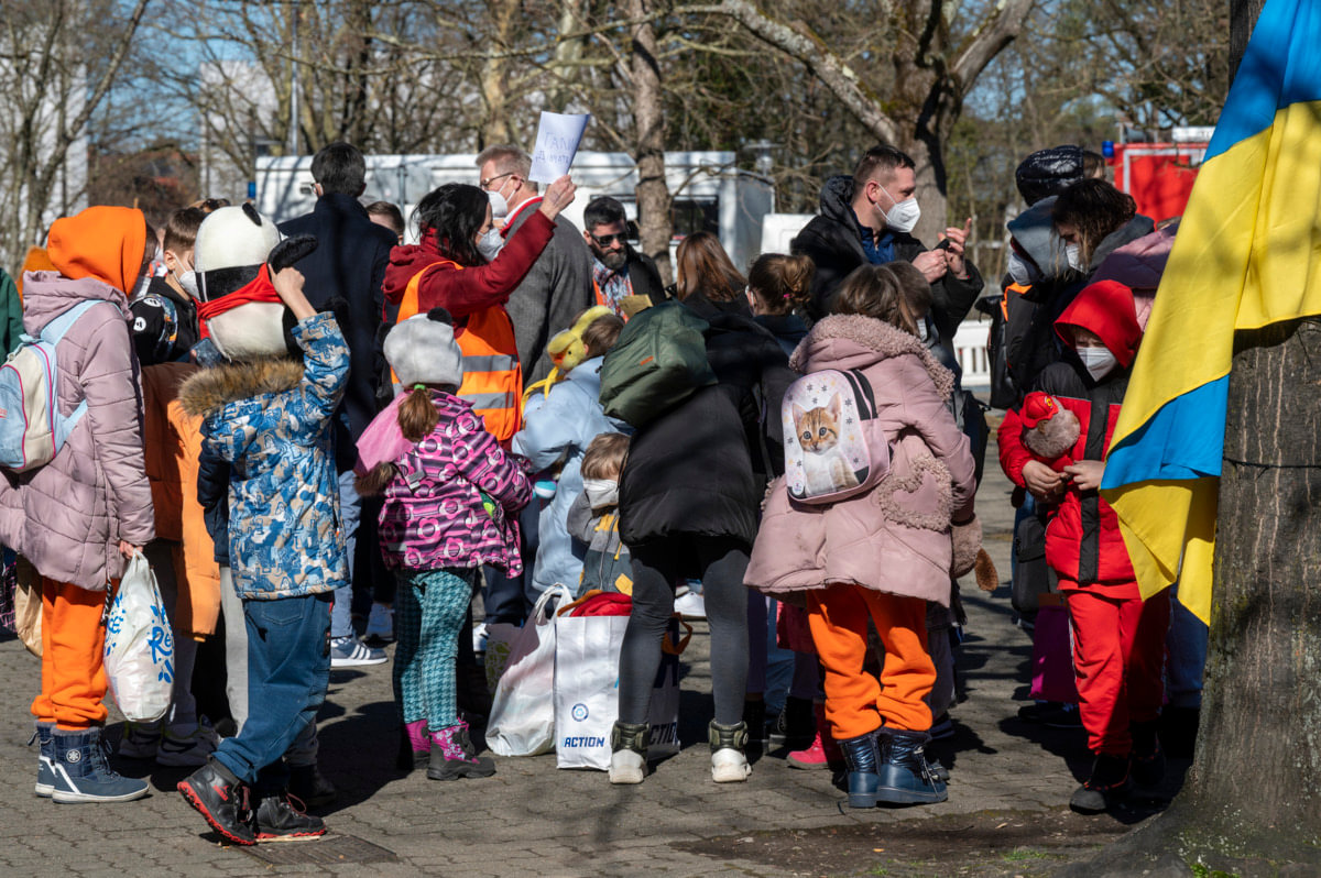 Geflüchtete ukrainische Kinder; auf der rechten Seite eine ukrainische Flagge an einem Baum.