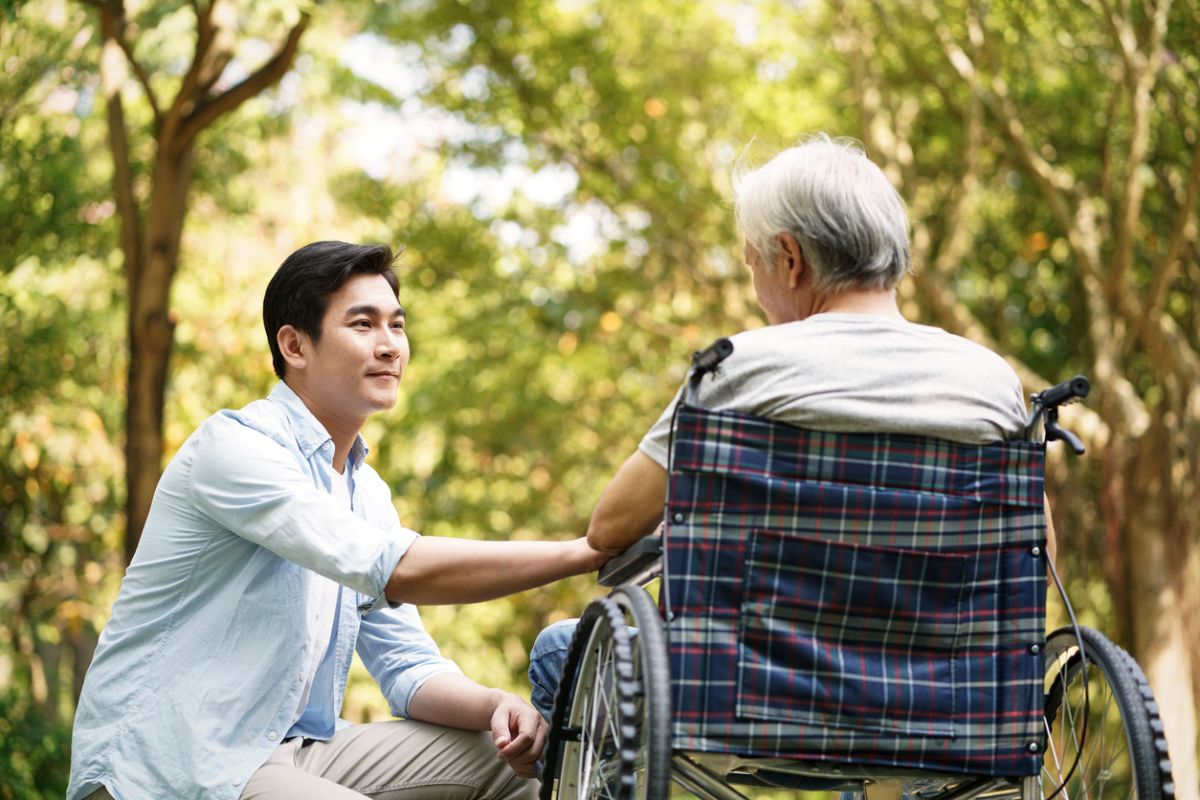 Junger Mann kniet vor einer älteren Person im Rollstuhl