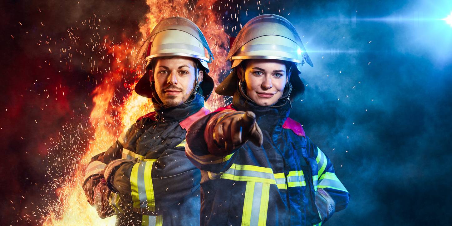 Ein Feuerwehrmann und eine Feuerwehrfrau vor einem rot-blauen Hintergrund mit Flammen