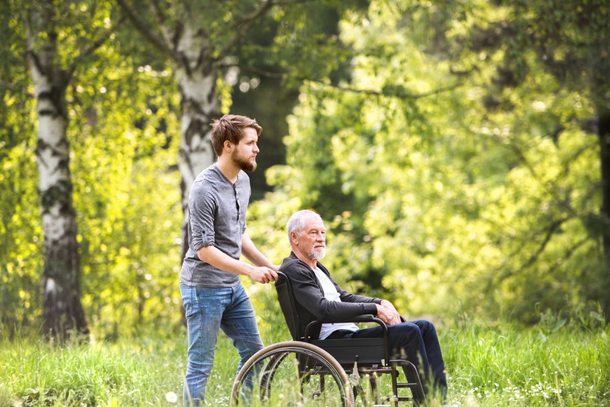 Ein junger Mann schiebt einen älteren Mann im Rollstuhl