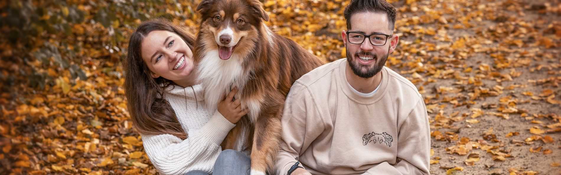 Eine junge Frau und ein junger Mann sitzen mit einem Hund auf Herbstlaub