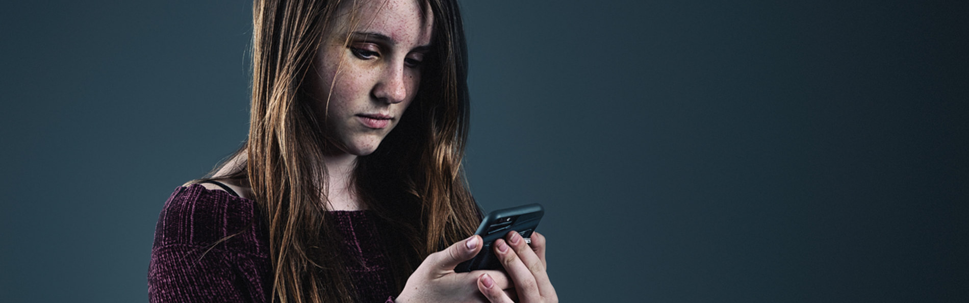 Junges Mädchen schaut mit resigniertem Gesichtsausdruck auf ein Smartphone