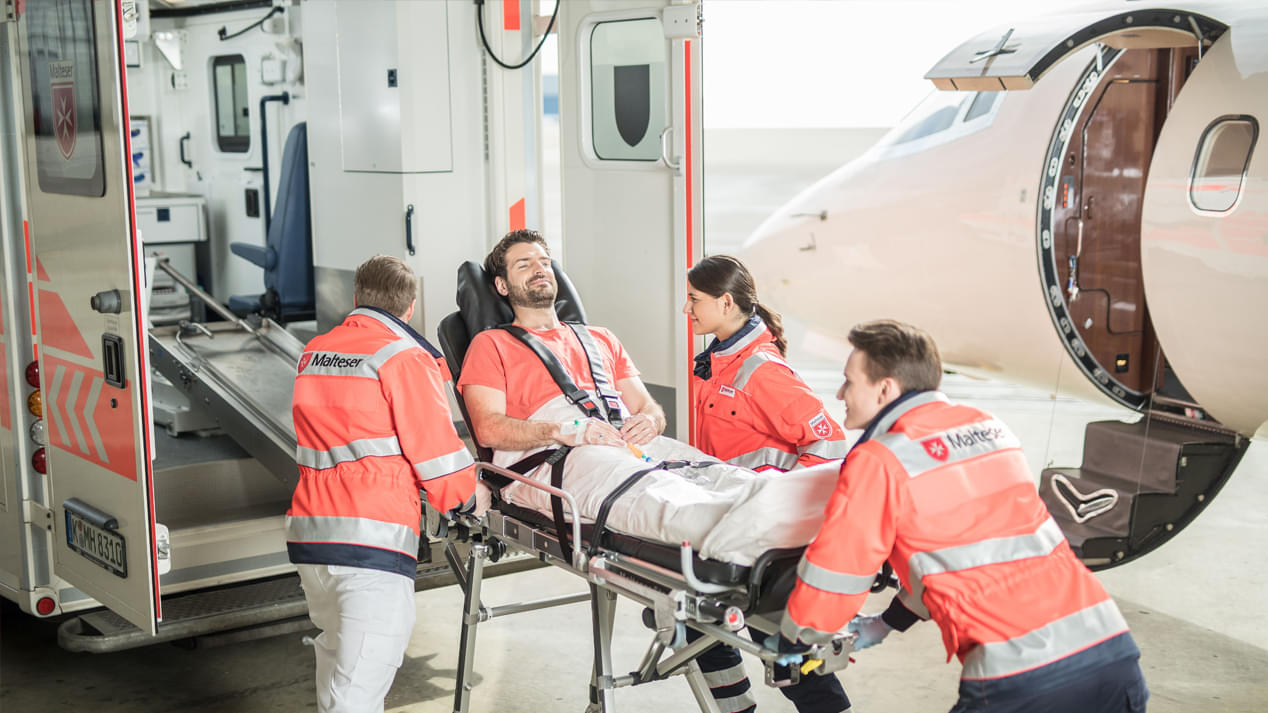Ein Mann wird von einem Flugzeug in einen Rettungswagen verladen