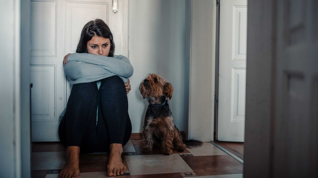 Eine junge Frau kauert mit einem Hund vor einer Tür