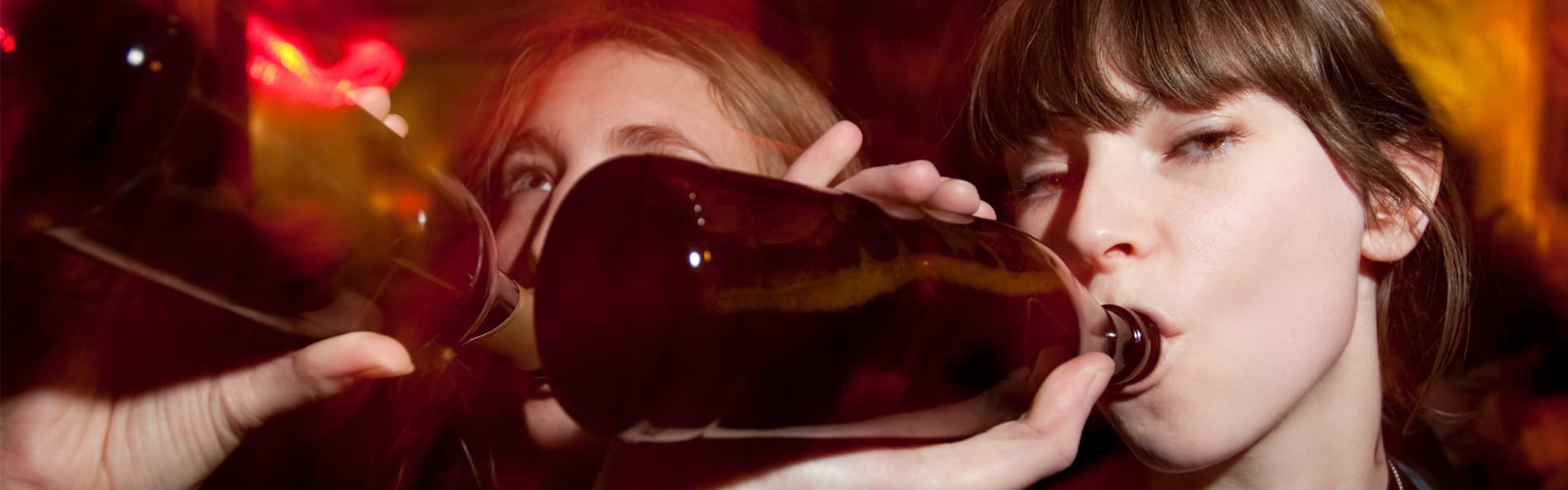Zwei junge Frauen trinken auf einer Party aus braunen Flaschen