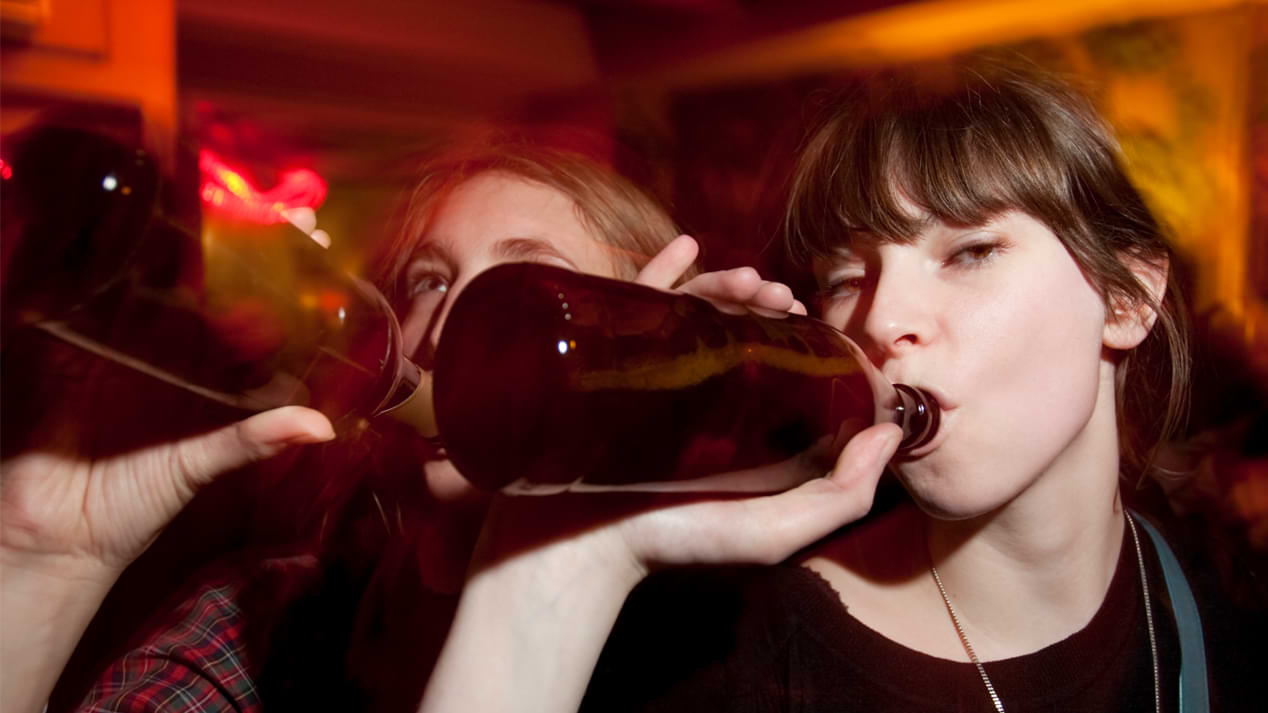 Zwei junge Frauen trinken auf einer Party aus braunen Flaschen