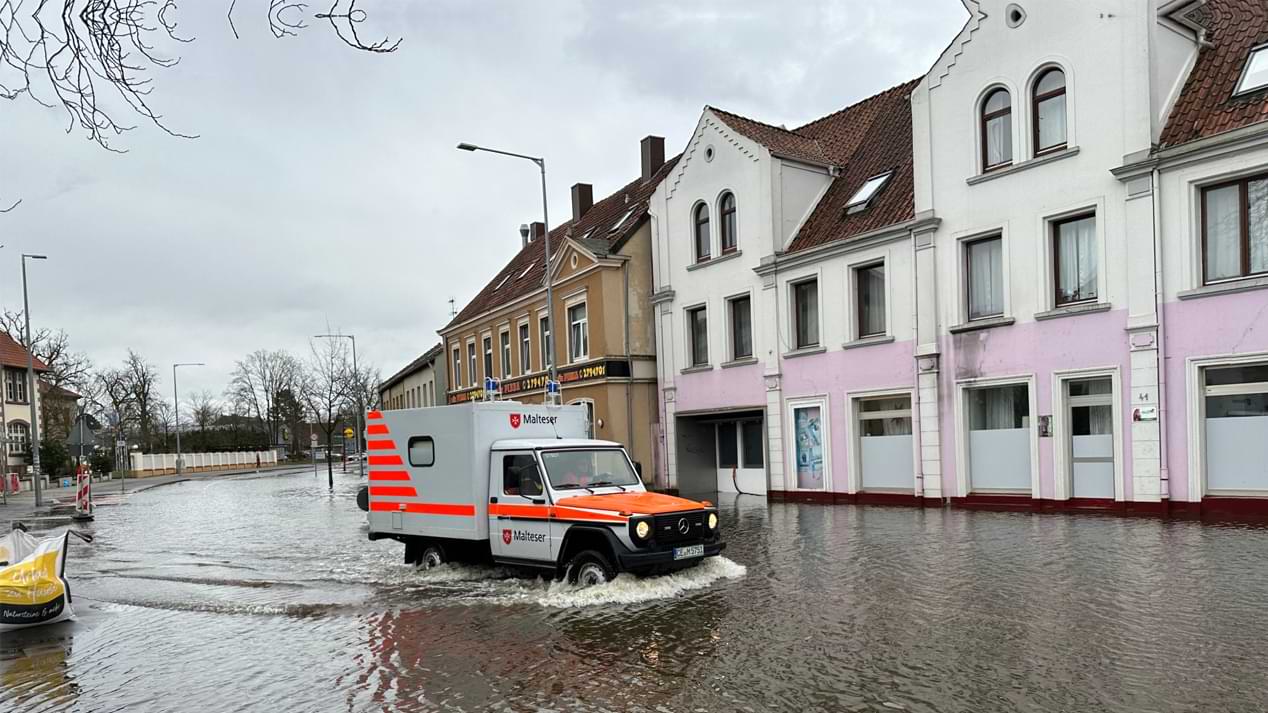 Ein Geländekrankenwagen der Malteser fährt über eine überschwemmte Straße
