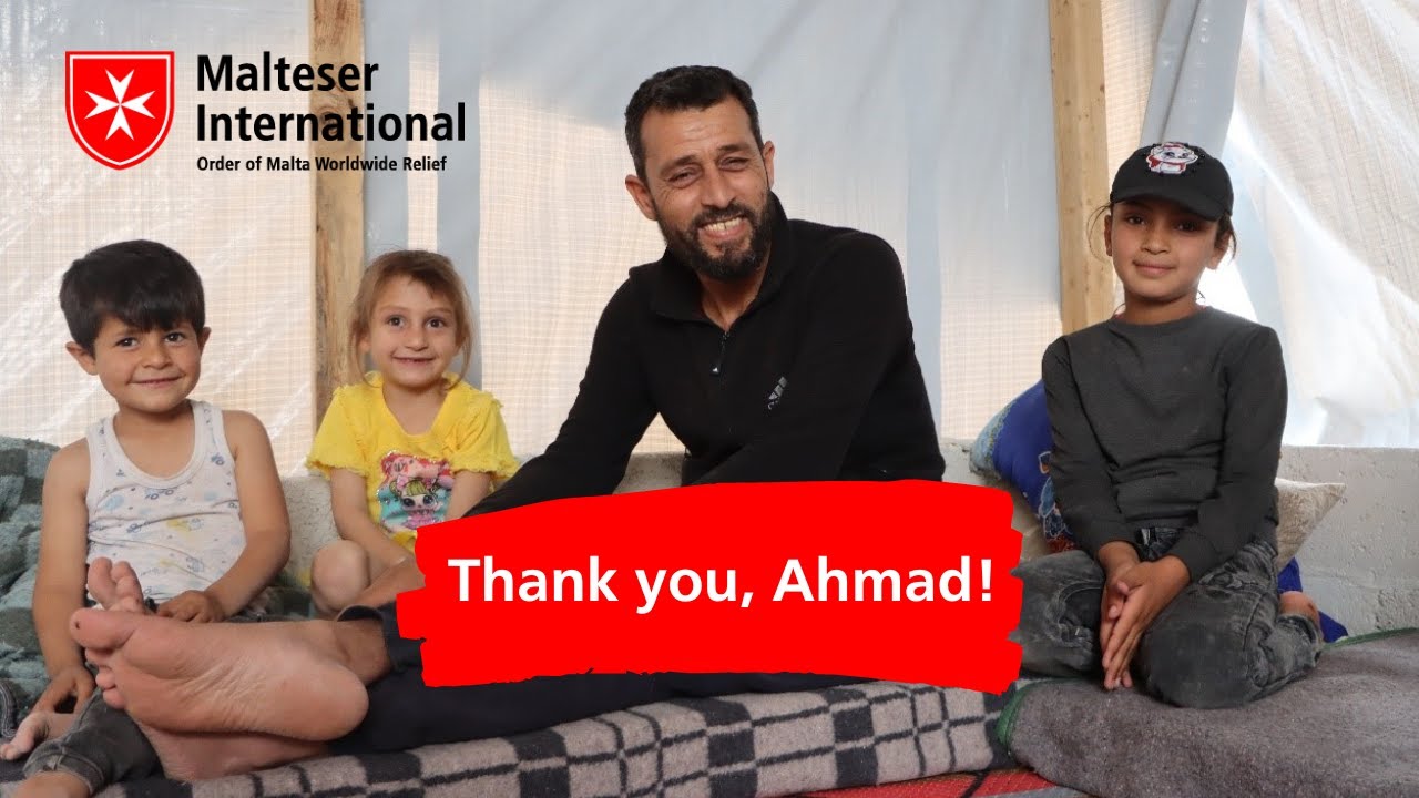 Ein Mann und drei Kimder sitzen auf einem Bett mit einem "Danke, Ahmad"-Banner.