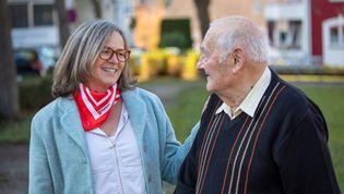 Eine Demenzbegleiterin und ein älterer Herr lachen gemeinsam im Freien.