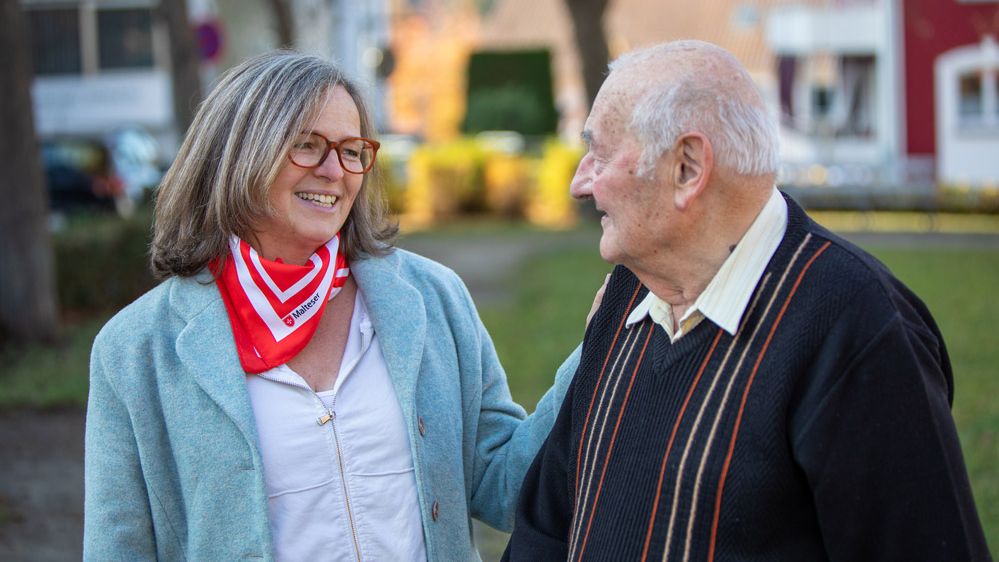 Eine Demenzbegleiterin und ein älterer Herr lachen gemeinsam im Freien.