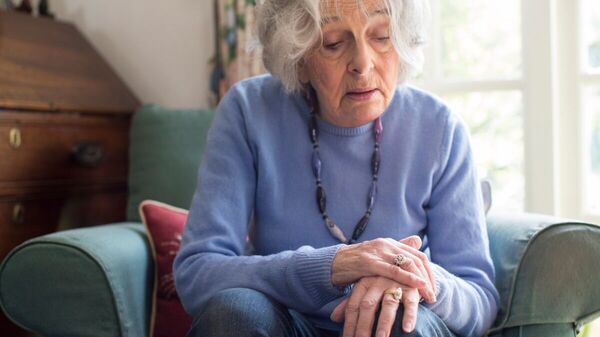 Eine ältere Frau auf einem Sessel schaut auf ihre Hände.