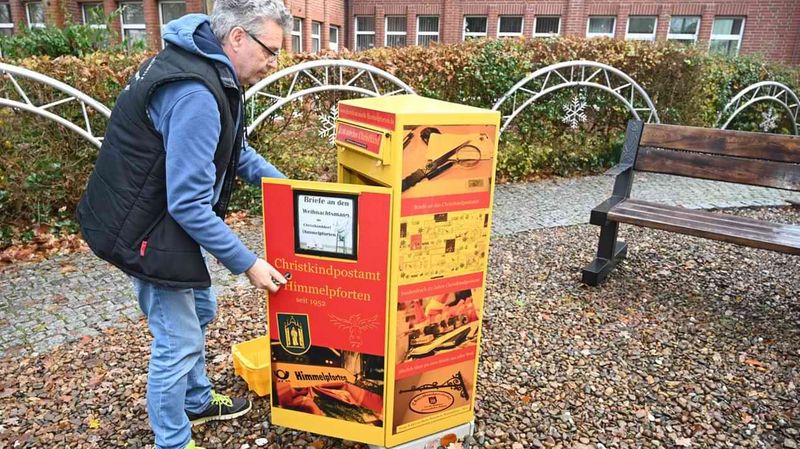 Ein Mann mit dunkler Weste öffnet einen Briefkasten der Deutschen Post