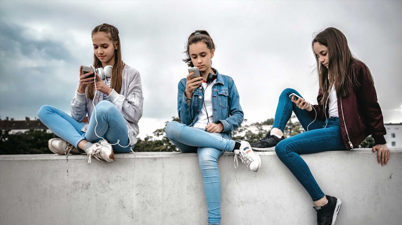 Drei Mädchen sitzen auf einer Betonmauer und schauen auf ihre Smartphones