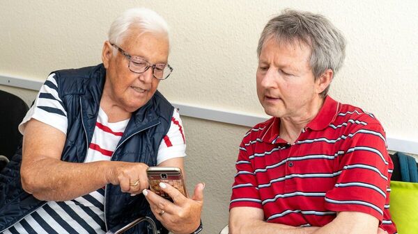 Ein Mann und eine ältere Frau mit Brille schauen auf ein Smartphone.