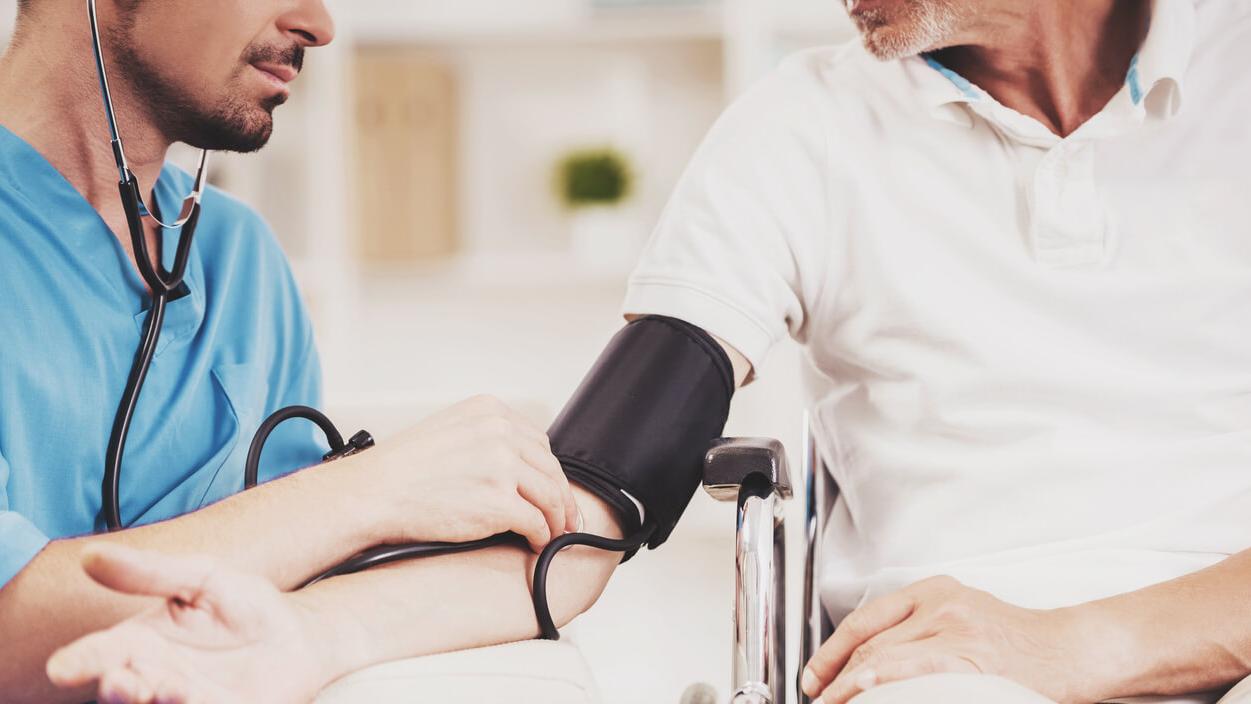 Ein Pfleger misst den Blutdruck eines älteren Rollstuhlfahrers.