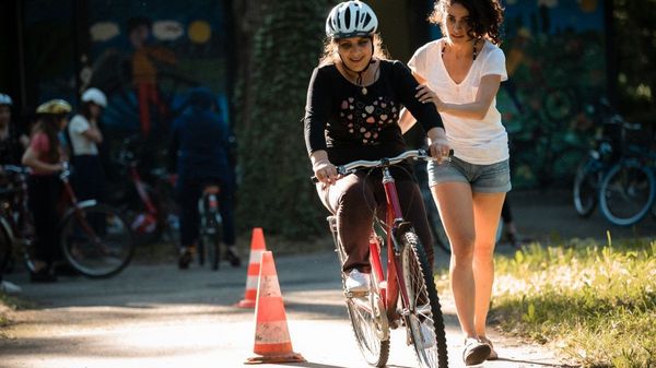 Eine junge Frau bringt einer anderen Frau Fahrradfahren bei. 