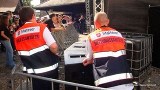 Zwei Malteser Einsatzsanitäter vor neben einer Bühne bei einem Konzert.